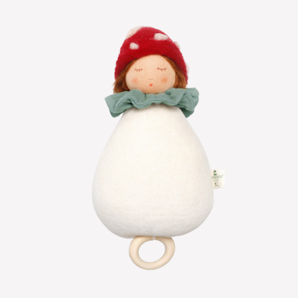 White teething ring with a red knit cap and green bow on a white background.  Rainbow Mushroom Girl Nanchen Natur Perfect for baby to drift of to fairytale dreamland with a sweet, soft, cuddly friend. Lovingly handmade to be just right for tiny hands to grasp and hold. Soothing, cozy, wonderfully soft and adorable to look at. Soft music will soothe and comfort. 